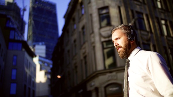 Hipster businessman with headphones walking on the street in London in the evening. Slow motion.