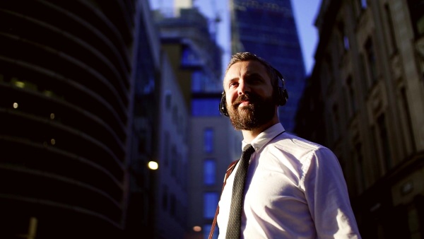 Hipster businessman with headphones standing on the street in London in the evening. Copy space. Slow motion.