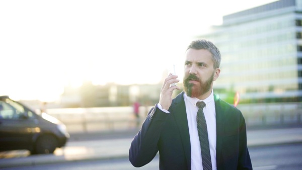 Hipster businessman with smartphone standing on the street in city, making a phone call. Slow motion.