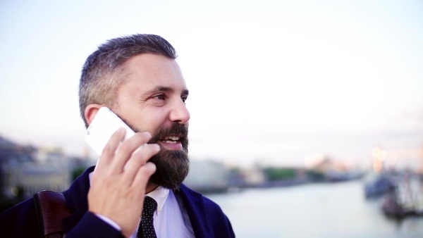 A close-up of a hipster businessman with smartphone standing on the bridge in the city, making a phone call. Slow motion.