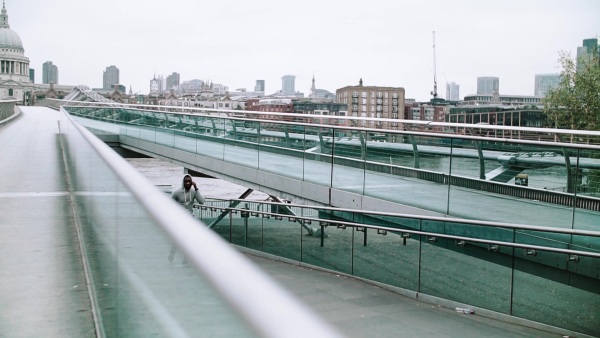 Young sporty black man runner with smart phone in arm band running on the bridge outside in a London city. Slow motion.