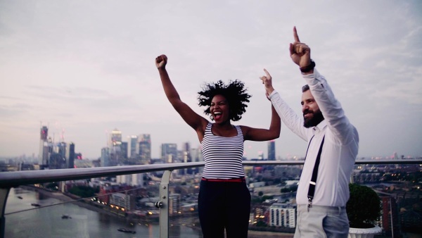 A portrait of businesspeople standing against London rooftop view panorama at sunset, laughing and expressing excitement. Slow motion.