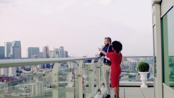 A full length view of two businesspeople standing against London rooftop view panorama, talking.