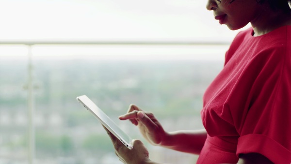 An unrecognizable woman standing by the window, using tablet. Copy space.