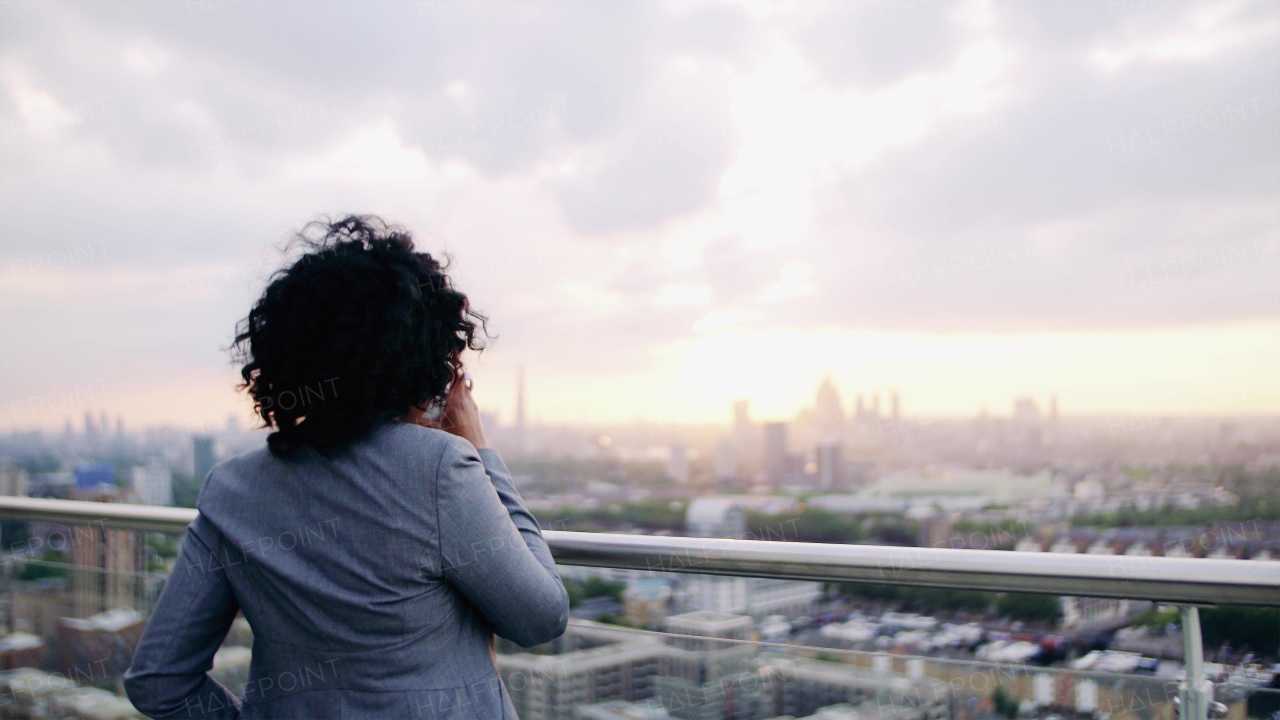 A rear view of black businesswoman standing on a terrace, drinking coffee.