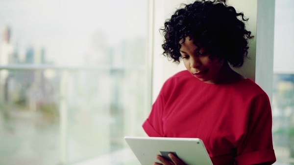 A portrait of woman standing by the window against London rooftop view panorama, using tablet. Copy space. Slow motion.