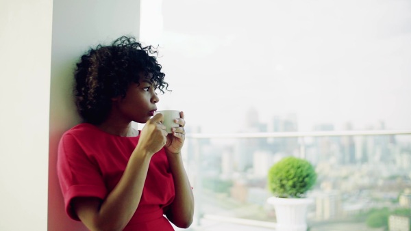 A portrait of woman standing by the window against London rooftop view panorama, drinking coffee. Copy space. Slow motion.