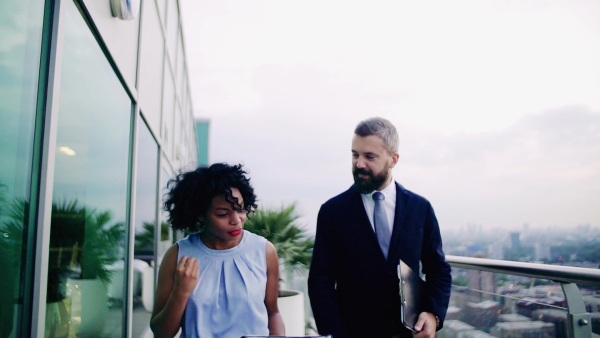 A portrait of businesspeople walking against London rooftop view, discussing something. Slow motion.