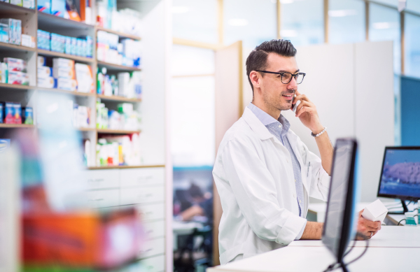 Portrait of a young atrractive friendly male pharmacist with a smartphone. Man making a phone call.