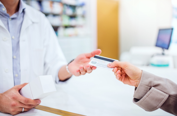 Unrecognizable male pharmacist serving a female customer. Credit or debit card payment.