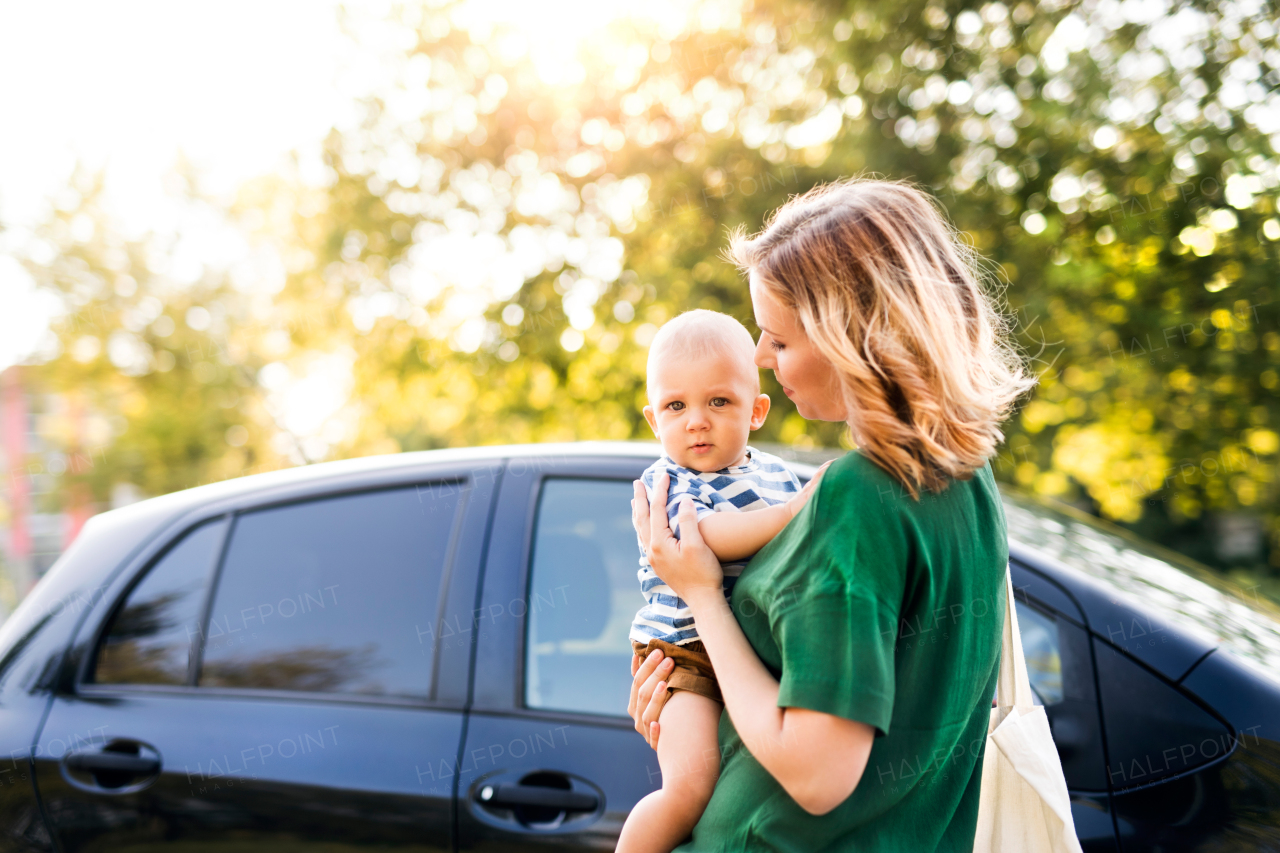 Young mother holding her little baby boy in the arms getting into the car.