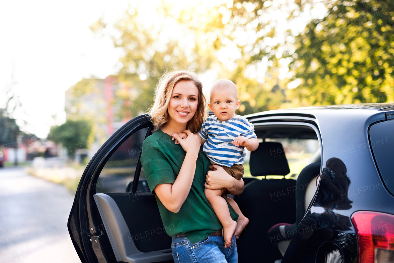 Young mother holding her little baby boy in the arms getting into the car.