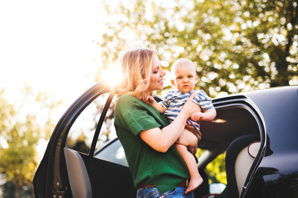 Young mother holding her little baby boy in the arms getting into the car.