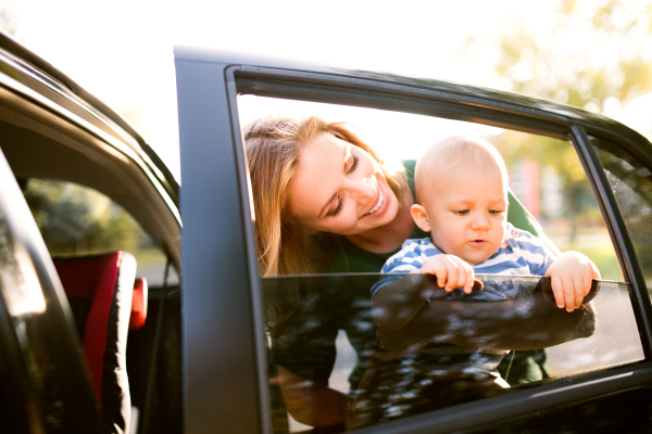 Young mother holding her little baby boy in the arms. Woman with son standing by the car.