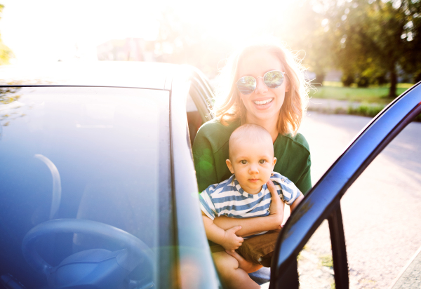 Young mother holding her little baby boy in the arms getting into the car.