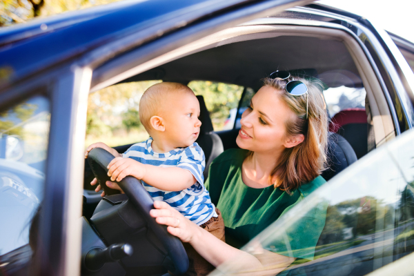 Young mother with her little son in the car. A woman and baby boy pretending to be driving.