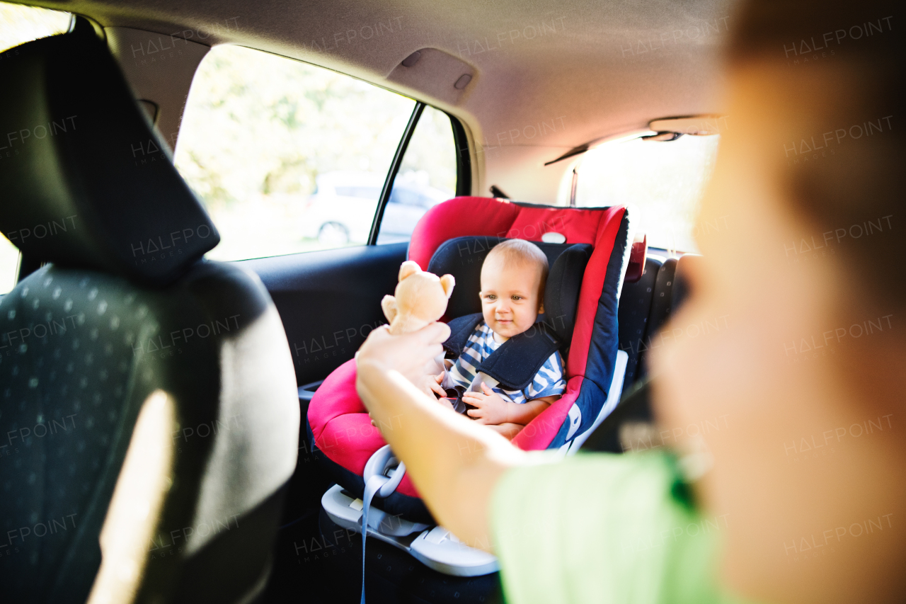 Young mother with her little son in the car. Baby boy sitting in a car seat, unrecognizable woman giving him a toy.