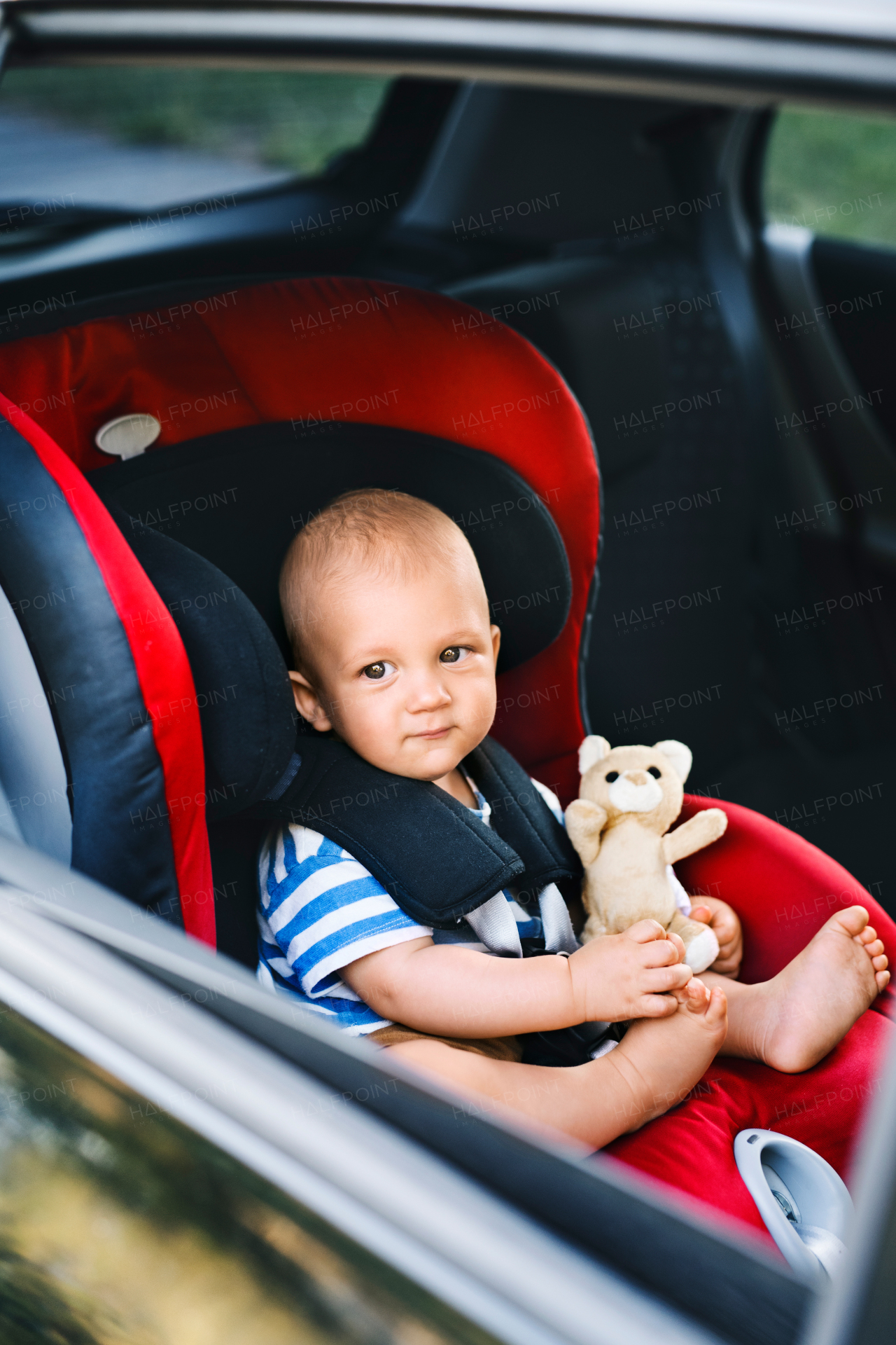 Cute little baby boy sitting in the car seat in the car, looking out.