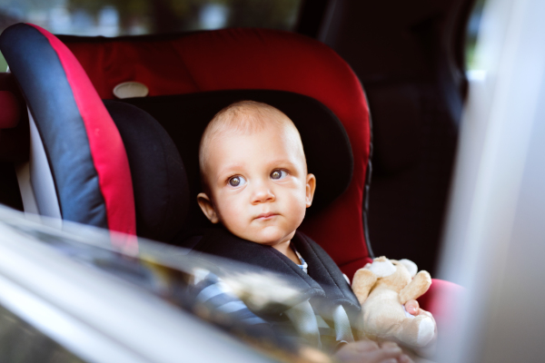 Cute little baby boy sitting in the car seat in the car, looking out. Close up.