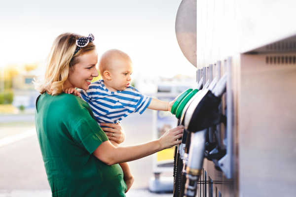 Young mother with baby boy at the petrol station going to refuel the car.