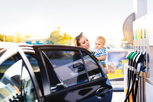 Young mother with baby boy at the petrol station going to refuel the car.