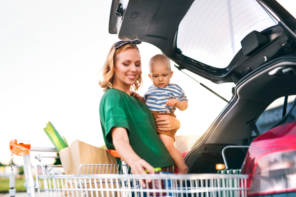 Beautiful young mother with baby boy putting shopping into back of car.