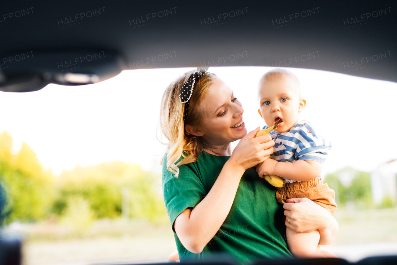 Young mother holding her little baby boy in the arms, standing by the open back of car.