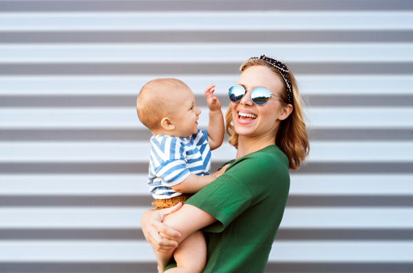 Young woman with a baby boy standing against the wall. Beautiful mother holding her son in arms.