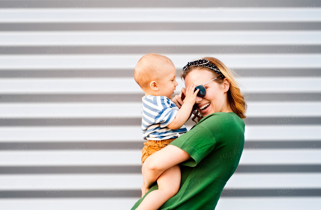 Young woman with a baby boy standing against the wall. Beautiful mother holding her son in arms.