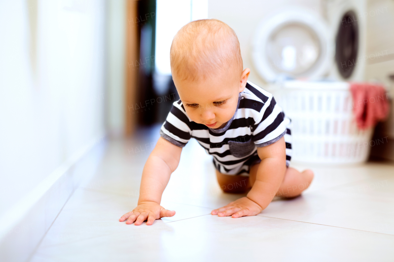 Baby boy by the washing mashine in the kitchen. Laundry basket on the floor.