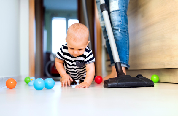 Unrecognizable young mother with a baby son doing housework. Beautiful woman and baby boy hoovering.