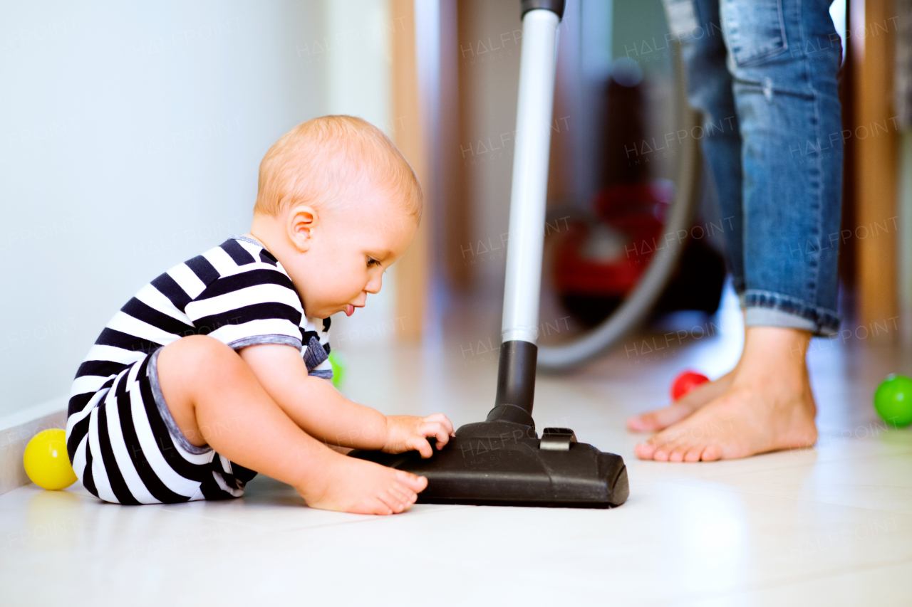 Unrecognizable young mother with a baby son doing housework. Beautiful woman and baby boy hoovering.