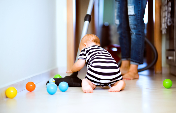 Unrecognizable young mother with a baby son doing housework. Beautiful woman and baby boy hoovering.