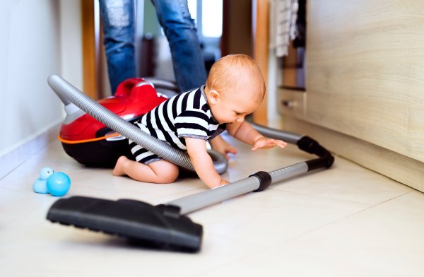 Unrecognizable young mother with a baby son doing housework. Beautiful woman and baby boy hoovering.