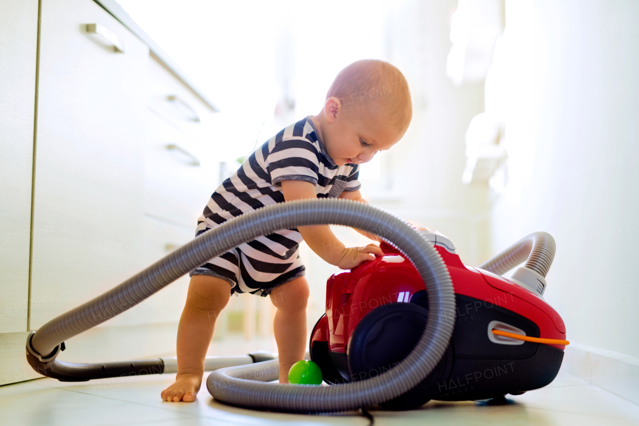 Cute baby boy with the hoover in the kitchen. Close up of a little boy playing with vacuum cleaner.