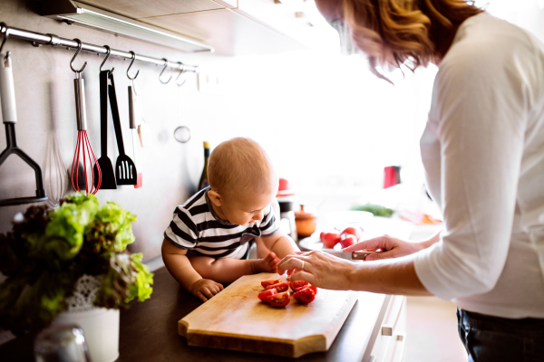 Unrecognizable young mother with a baby son doing housework. Beautiful woman and baby boy cooking in the kitchen.