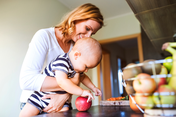 Young mother with a baby son doing housework. Beautiful woman and baby boy in the kitchen.