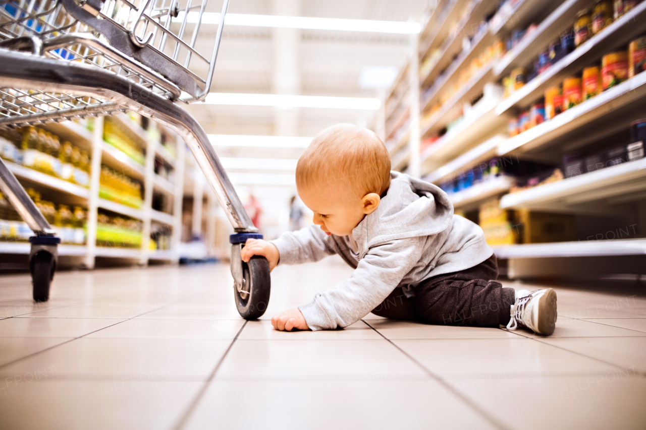 Cute little baby at the supermarket. Baby on the floor, next to shopping trolley.