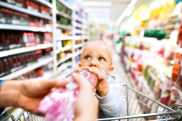 Unrecognizable young mother with her little baby boy at the supermarket, shopping. Toddler drinking.