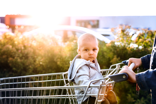 Unrecognizable mother with baby boy going shopping in the car park. Toddler boy sitting in a shopping trolley.