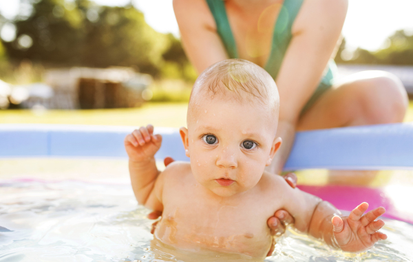 Little baby boy with his unrecognizable mother in the swimming pool in the garden. Summer time.