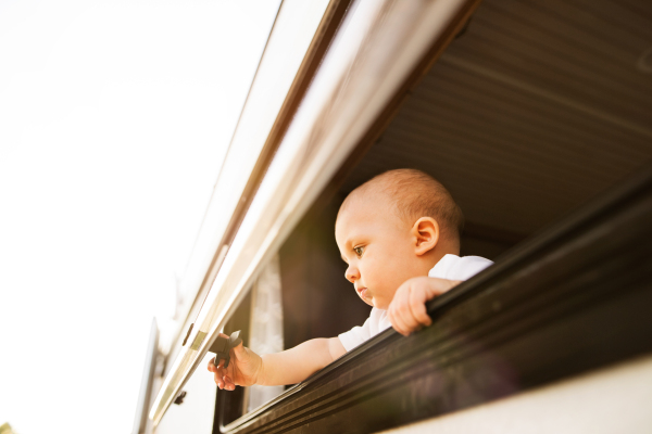 Gorgeous baby boy in a camper van on a summer day. Little boy opening the window.