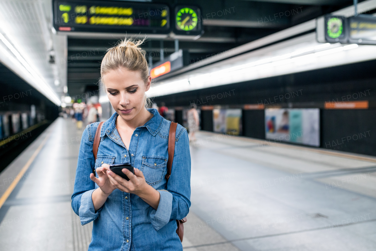 Beautiful young woman in denim shirt with smart phone, standing at the underground platform, texting