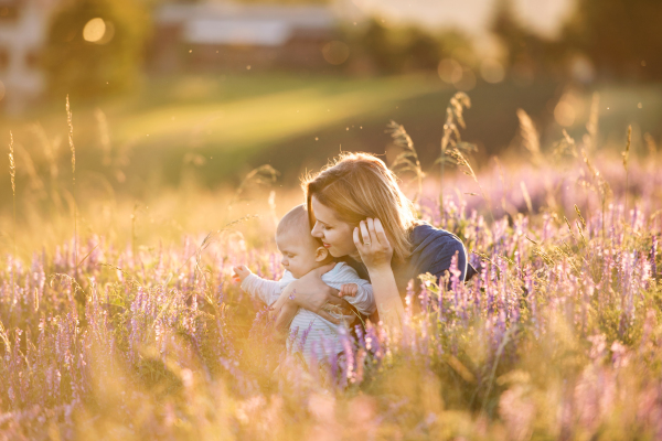 Beautiful young mother holding her little baby son in the arms outdoors in nature in lavender field.