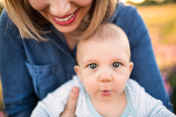 Unrecognizable young mother holding her little baby son in the arms outdoors in nature.