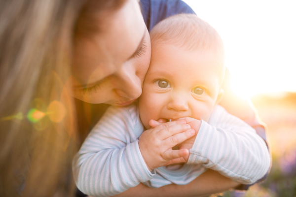 Unrecognizable young mother holding her little baby son in the arms outdoors in nature.