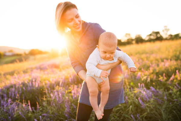 Beautiful young mother holding her little baby son in the arms outdoors in nature in lavender field.