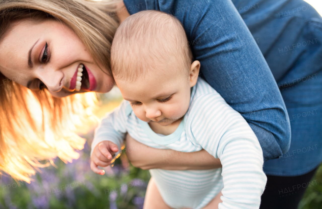 Beautiful young mother holding her little baby son in the arms outdoors in nature in lavender field.