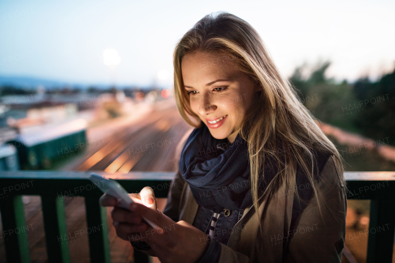 Beautiful woman in the city at night holding smartphone, texting.