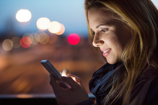 Beautiful woman in the city at night holding smartphone, texting.